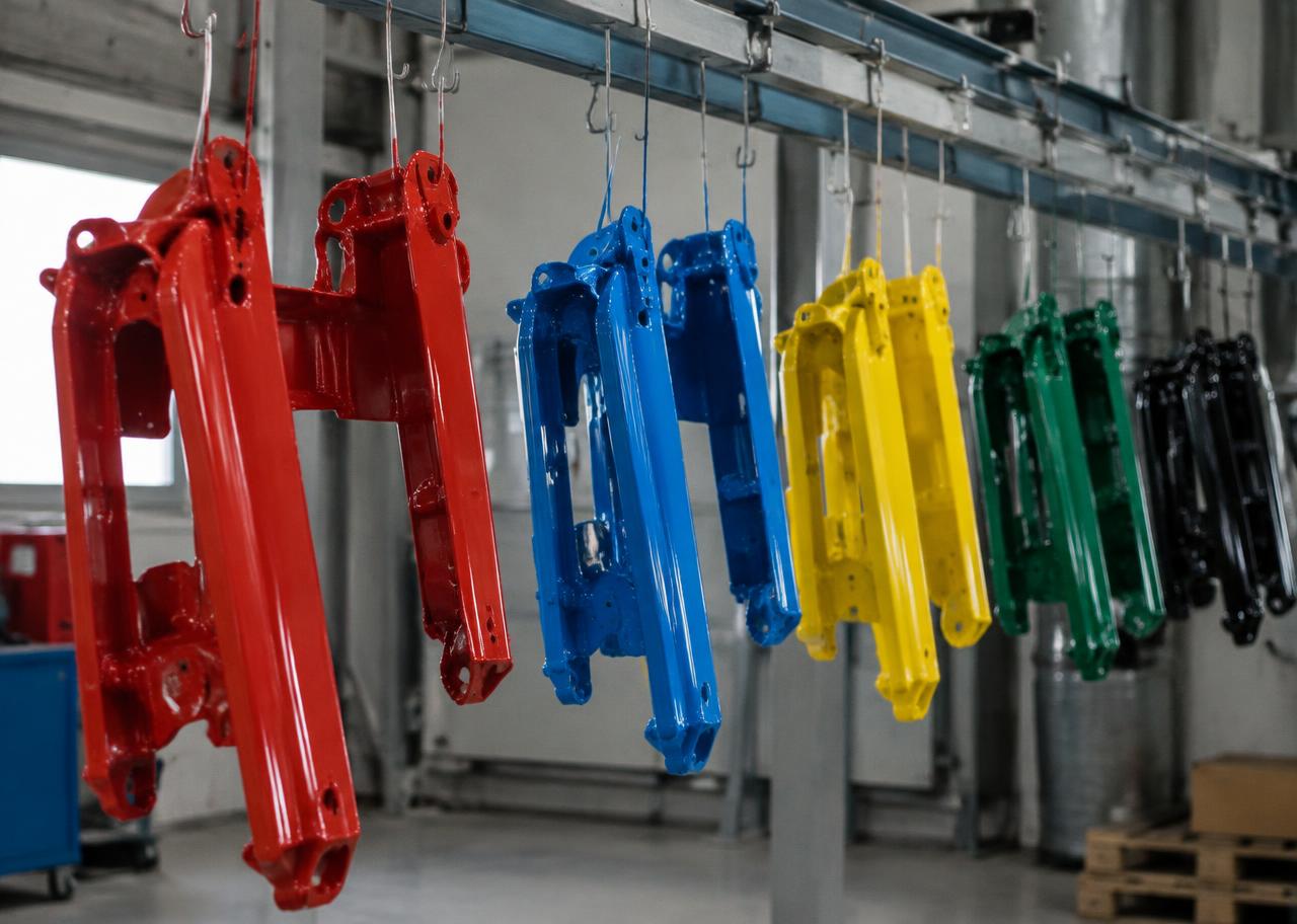 Pezzi metallici appena verniciati a polvere appesi al trasportatore in rosso, blu, giallo, verde e nero